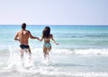 Happy cheerful couple hold hans and running in the sea together. Romantic vacation, honeymoon love Royalty Free Stock Photo