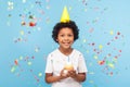 Happy cheerful cute little boy with funny party cone on head holding cupcake and smiling while confetti falling Royalty Free Stock Photo
