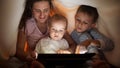 Happy cheerful family hiding under blanket and using tablet computer. Family having time together, parenting, happy childhood and Royalty Free Stock Photo