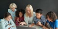 Happy teacher sitting together with diverse schoolkids at desk using laptop. Royalty Free Stock Photo