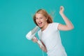 A happy cheerful girl dries her hair with a hair dryer and sings using the hair dryer as a microphone. Blue mint background, Royalty Free Stock Photo