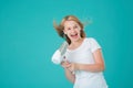 A happy cheerful girl dries her hair with a hair dryer and sings using the hair dryer as a microphone. Blue mint background, Royalty Free Stock Photo