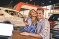 Happy cheerful girl getting a car key with handsome man in auto salon. Business concept and car selling Royalty Free Stock Photo