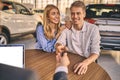 Happy cheerful girl getting a car key with handsome man in showroom. Business concept and car selling Royalty Free Stock Photo