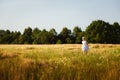 A happy and cheerful girl in a white sundress and hat runs across the field at sunset. A little girl runs in the summer on a rural Royalty Free Stock Photo