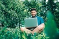 Happy cheerful hipster man with a laptop sitting outdoors on green grass Royalty Free Stock Photo