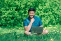 Happy cheerful hipster man with a laptop sitting outdoors on green grass Royalty Free Stock Photo