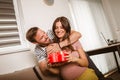 Happy cheerful husband giving present box to his pregnant wife Royalty Free Stock Photo