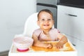 happy cheerful messy baby sits in a highchair and eats lure vegetable puree soup, the concept of baby food