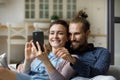 Happy cheerful millennial couple taking selfie on couch at home