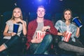 Happy and cheerful people are sitting and watching movie. They are excited. Blonde girl has a cup of cola. Guy holds a Royalty Free Stock Photo