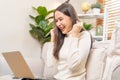 Happy cheerful, satisfied asian young freelancer woman, girl sitting on sofa or couch, using laptop computer in living room at