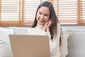 Happy cheerful, satisfied asian young freelancer woman, girl sitting on sofa or couch, using laptop computer in living room at Royalty Free Stock Photo