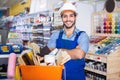 Workman standing folded arms near basket with picked tools in paint store