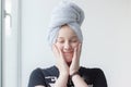 A happy and cheerful teenage girl with white, clear skin and a blue towel on her head closed her eyes and pressed her hands to her