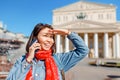 Cheerful traveler girl talking by phone at the Bolshoi Theatre in the background