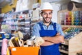 Workman standing folded arms near basket with picked tools in paint store