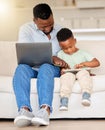 Happy cheerful young african american man using a laptop while helping his son with a digital tablet sitting on the Royalty Free Stock Photo