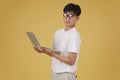 Happy cheerful young asian man nerd student dressed casually wearing eyeglasses holding laptop computer isolated on yellow Royalty Free Stock Photo