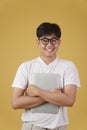 Happy cheerful young asian man nerd student dressed casually wearing eyeglasses holding laptop computer isolated on yellow Royalty Free Stock Photo