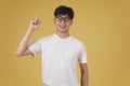 Happy cheerful young asian man student dressed casually wearing eyeglasses pointing finger up having idea isolated on yellow Royalty Free Stock Photo