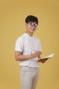 Happy young asian man student dressed casually wearing eyeglasses writing note isolated on yellow studio background Royalty Free Stock Photo