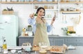 Happy cheerful young asian woman raise smartphone fist good mood wear headphones listen to music in kitchen at home Royalty Free Stock Photo