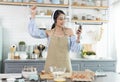 Happy cheerful young asian woman raise smartphone fist good mood wear headphones listen to music in kitchen at home Royalty Free Stock Photo