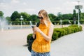 Happy cheerful young blond woman with backpack walking on city street checks her smartphone. Portrait of beautiful 30s Royalty Free Stock Photo