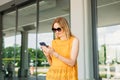 Happy cheerful young blond woman in sunglasses walking on city street checks her smartphone. Portrait of beautiful 30s Royalty Free Stock Photo