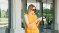 Happy cheerful young blond woman in sunglasses walking on city street checks her smartphone. Portrait of beautiful 30s Royalty Free Stock Photo