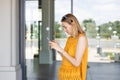 Happy cheerful young blond woman walking on city street checks her smartphone. Portrait of beautiful girl using Royalty Free Stock Photo