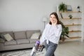 Happy cheerful young Caucasian beautiful woman vacuuming floor and using smartphone at home in living room, domestic concept Royalty Free Stock Photo