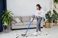 Happy cheerful young Caucasian beautiful woman vacuuming floor and using smartphone at home in living room, domestic concept Royalty Free Stock Photo