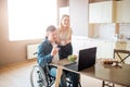 Happy cheerful young man sit at table and look on laptop. Guy with disability and inclusiveness. Young woman stand Royalty Free Stock Photo