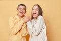 Happy cheerful young man and woman couple standing together isolated over beige background holding hands and laughing happily Royalty Free Stock Photo