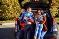 Happy cheerful young parents sitting in the car`s trunk and hug their happy kids running to them. Royalty Free Stock Photo