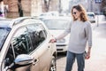 Happy cheerful young woman driver in sunlasses opens her car with a remote key on the street in the city Royalty Free Stock Photo