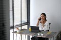 Happy cheerful young woman making answering call by cellphone while sitting in her office. Royalty Free Stock Photo