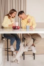 Happy cherrful couple in the kitchen sitting by the table and drinking from the cups, dog under the table
