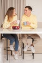 Happy cherrful couple in the kitchen sitting by the table and drinking from the cups