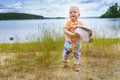 Happy child walks along the shore of a forest lake on a background of blue clouds on a summer day