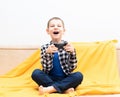 Happy child boy in checked shirt sitting on the couch with black joystick in his hands playing the video game. Playing Royalty Free Stock Photo