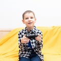 Happy child boy in checked shirt sitting on the couch with black joystick in his hands playing the video game. Playing Royalty Free Stock Photo