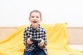 Happy child boy in checked shirt sitting on the couch with black joystick in his hands playing the video game. Playing Royalty Free Stock Photo