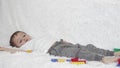 Happy child boy playing lying on white couch, against a background of colored toys, moving legs.