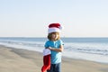 Happy child boy in Santa Claus hat on sea beach. Hot New Year. Cute baby boy in red Santa hat with christmas stocking on Royalty Free Stock Photo