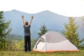 Happy child boy standing with raised hands near a tourist tent at mountain campsite enjoying view of beautiful summer nature. Royalty Free Stock Photo