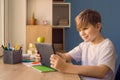 Happy child boy talking to his teacher or friend on tablet, doing homework at home Royalty Free Stock Photo