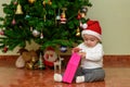 Happy child with a Christmas gift. Joyful baby at home opening a little gift while sitting in front of a Christmas tree. Royalty Free Stock Photo